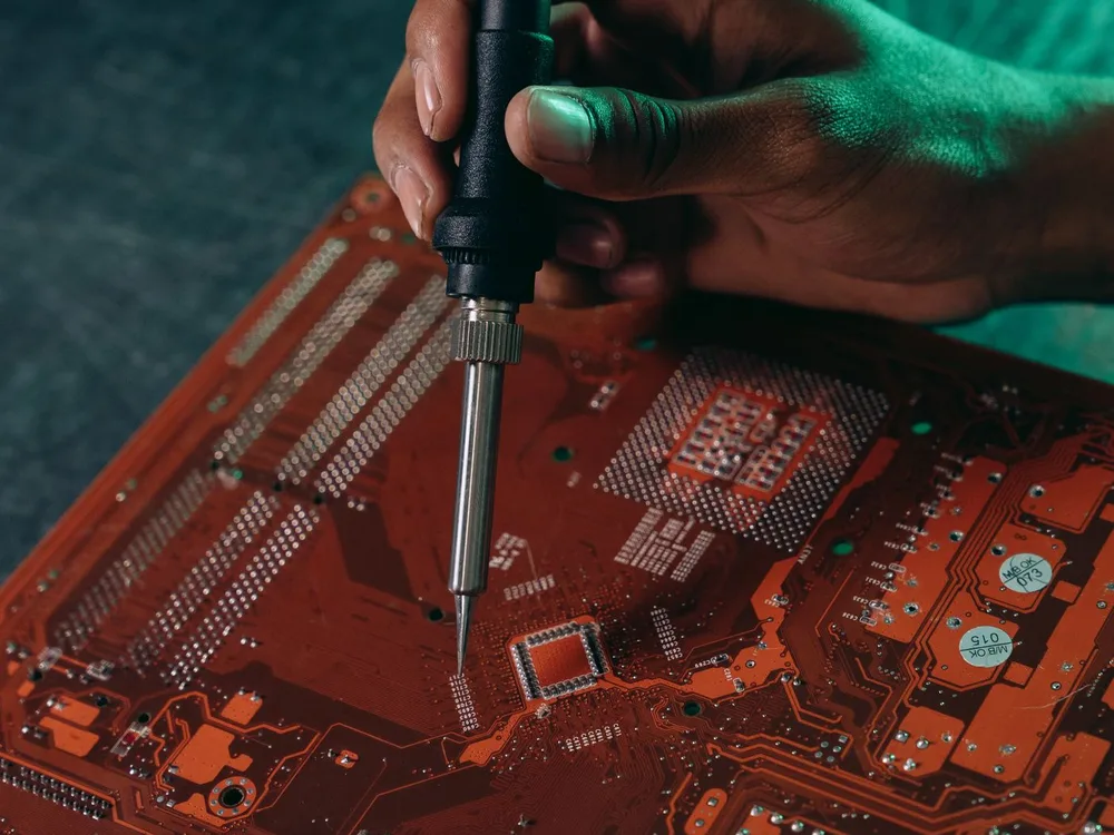 Técnico soldando con cautín un componente sobre la placa electrónica de un equipo