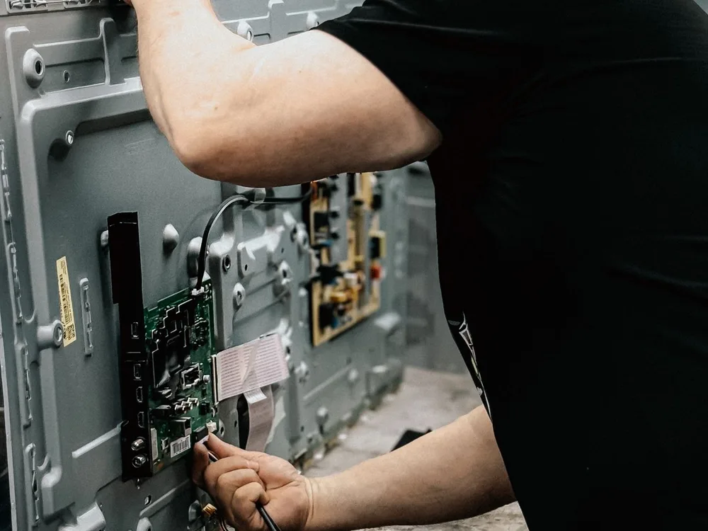 Técnico reparando un televisor abierto con la fuente de poder y las tarjetas electrónicas a la vista